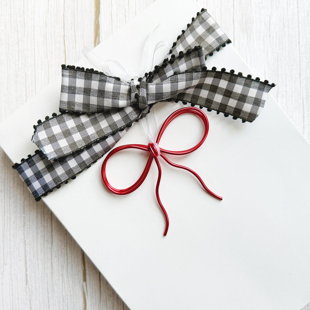 Red wire bow tied onto a holiday gift with black and white ribbon