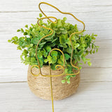 Gold wire bunny plant stake leaning against a faux decorative plant with green leaves on a light wood background.