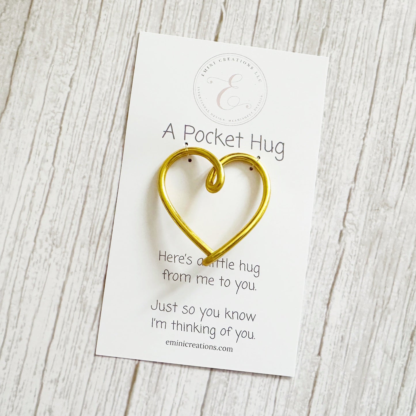 Gold heart-shaped pocket hug on a white branded card with text on a wooden surface
