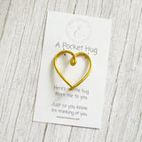 Gold heart-shaped pocket hug on a white branded card with text on a wooden surface