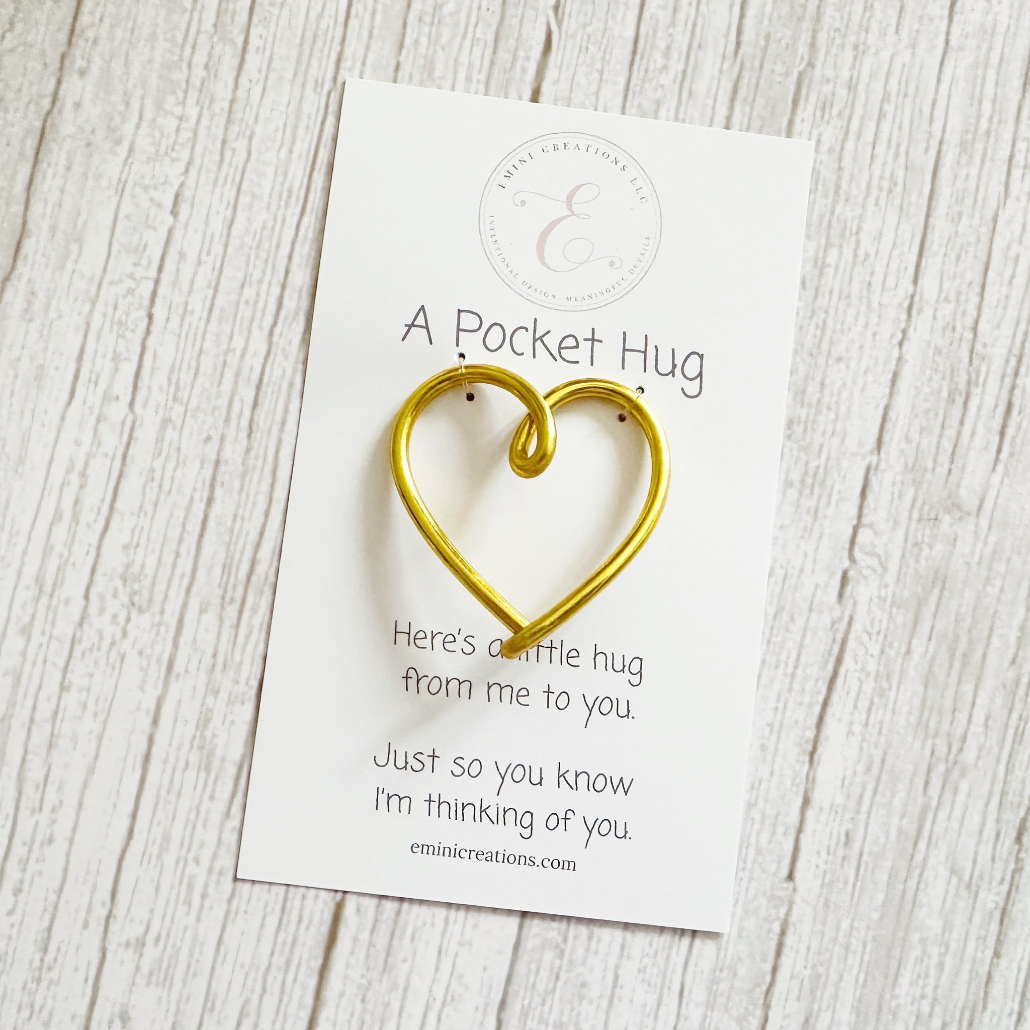 Gold heart-shaped pocket hug on a white branded card with text on a wooden surface