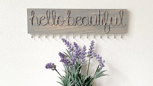 Hello Beautiful wire word on gray wooden plank with silver hooks to hang and organize jewelry.