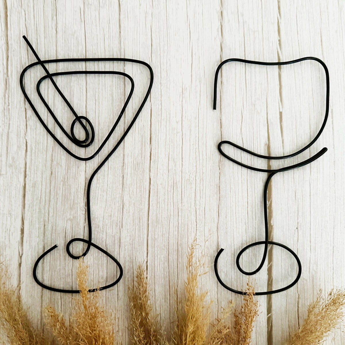 Decorative black wire martini glass and wine glass on a wooden background with brown dried grasses.