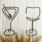 Decorative black wire martini glass and wine glass on a wooden background with brown dried grasses.