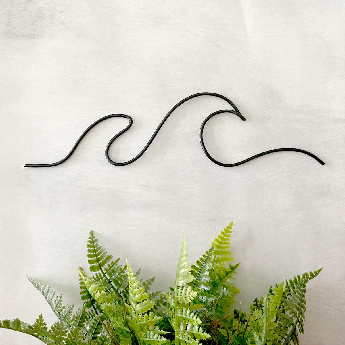 Black wire bent into one small and one large wave for home wall decor.